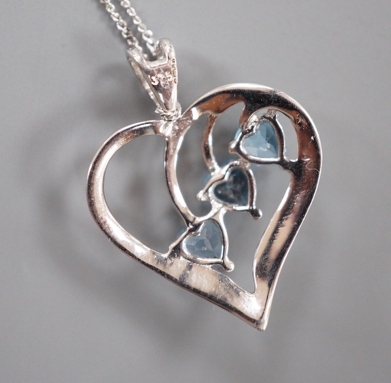 A modern 9ct white gold and three stone blue topaz set stylised heart shaped, pendant, 25mm, on a 375 fine link chain, 40cm, gross weight 2.7 grams.